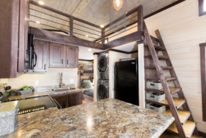 Interior of a compact kitchen with wooden cabinets, granite countertops, and modern appliances, featuring a loft ladder leading to an upper level.