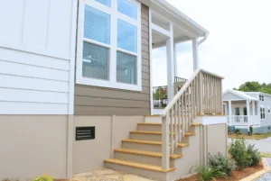 Exterior view of a modern home with white and gray siding, featuring a small porch with wooden stairs and a handrail.