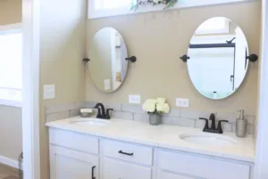 Modern bathroom with dual sinks, round mirrors, white cabinetry, and marble countertops, decorated with flowers.