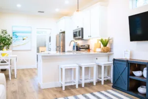 Bright, modern kitchen with white cabinetry, a central island with bar stools, hardwood floors, and coastal-themed decor.