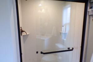 Interior view of a modern bathroom with a glass shower door, visible toilet, and a sink by a window.