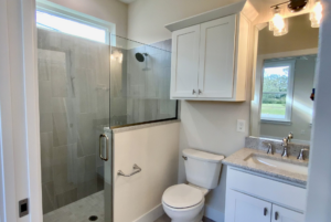 Modern bathroom with glass shower enclosure, white cabinetry, and mirror over a sink, viewed from the doorway.