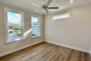 Empty room with hardwood floors, three windows, and a ceiling fan, offering natural light and a view of the outside.