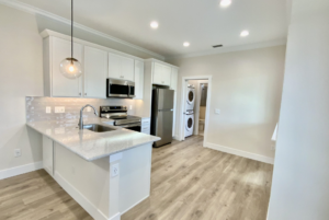 Modern kitchen with white cabinets, stainless steel appliances, and an island, leading to a laundry area with washer and dryer.