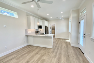 Spacious, modern kitchen with white cabinetry, stainless steel appliances, and light wooden flooring, featuring a central island and pendant lighting.