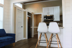 Modern kitchen with two white bar stools at a counter, blue sofa to the left, and white cabinets in back.