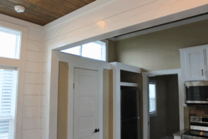 White paneled kitchen with a wooden ceiling, modern appliances, and doors leading to other rooms.