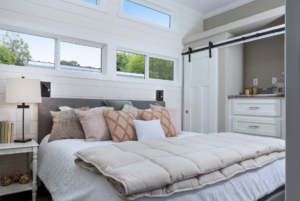 Modern bedroom with a king-size bed, pastel bedding, sliding barn door, and large horizontal windows above the bed.