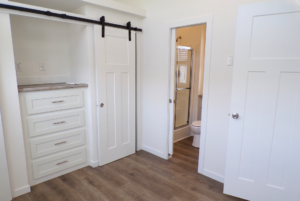 A modern laundry room with white cabinetry and a sliding barn door, leading to a visible bathroom with a toilet.