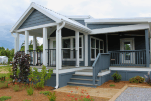 Modern blue swayback house with white trim, 2 beds, front porch, steps, railing, and landscaped garden.