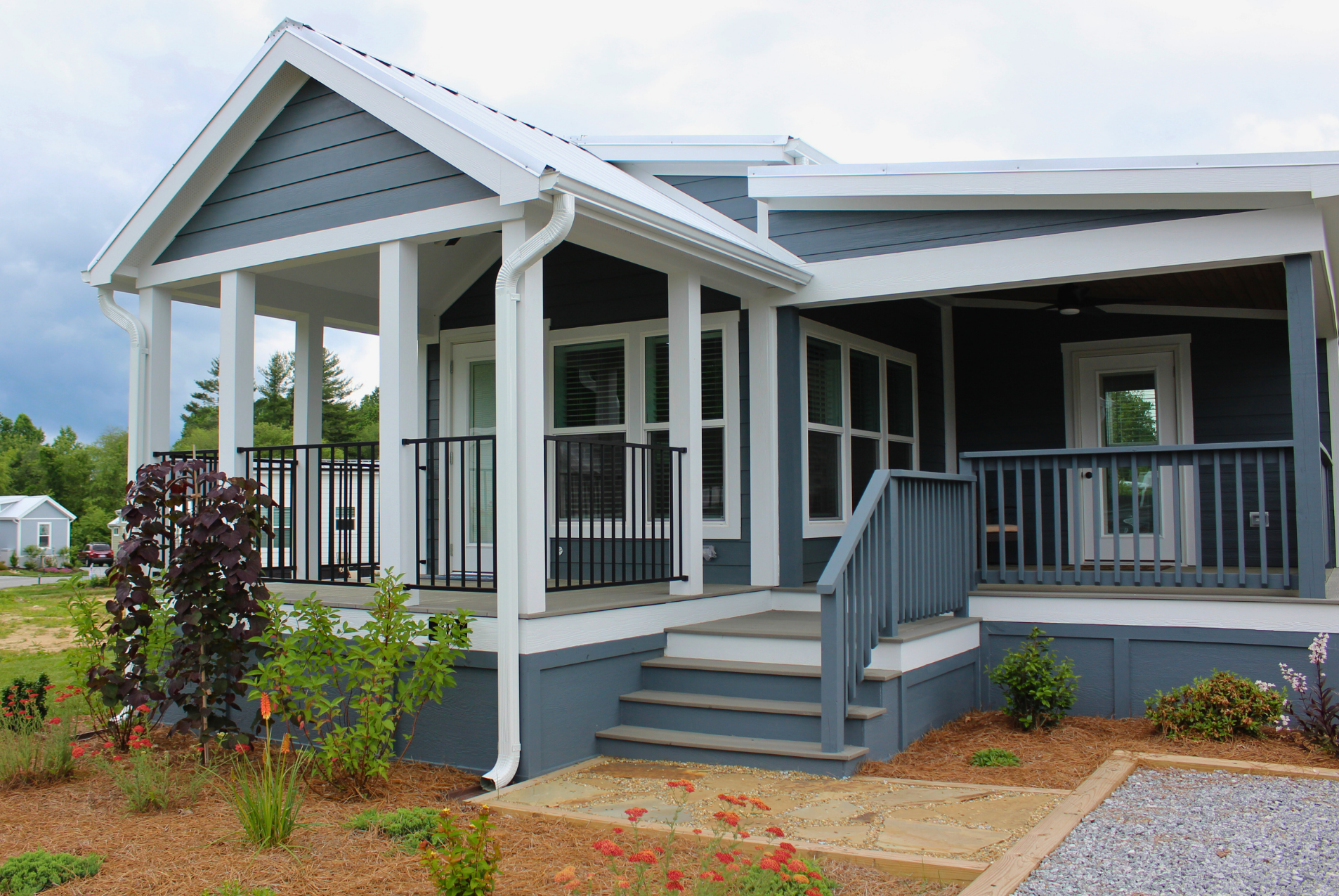 Modern blue swayback house with white trim, 2 beds, front porch, steps, railing, and landscaped garden.