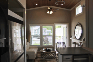 Modern, cozy living room with couch, round coffee table, windows, bar stools, and 2 beds nearby.