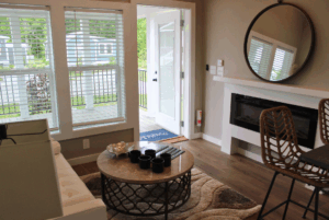 Modern living room with large windows, 2 beds nearby, round mirror, and open door to porch with neutral decor.