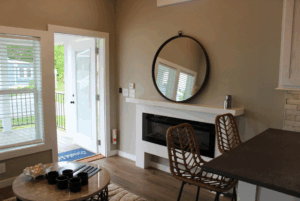 Modern living area with wicker chairs, a swayback fireplace, round mirror, and open door to porch. 2 beds included.