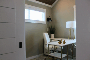 Modern home office with a white desk, gold duck decor, and a swayback chair by the window. 2 beds nearby.