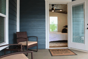 Cozy porch with two chairs, an open door to a 2 Beds bedroom; doormat reads, Simple Life: Live large. Carry less.