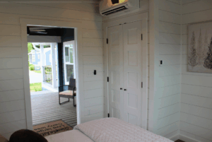 Bedroom with white paneled walls, 2 beds, closet, and an open door leading to a porch with a chair outside.