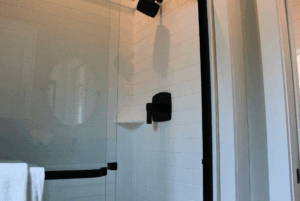 Modern shower with glass door, black fixtures, subway tiles, and a white towel—nearby, 2 beds await your swayback rest.