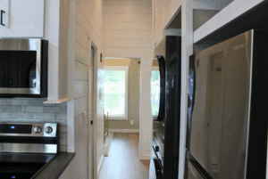 Narrow modern kitchen with stainless steel appliances leads to bright room; 2 beds in adjacent swayback-style layout.