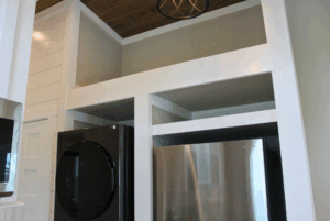 A black washing machine and a silver refrigerator sit side by side in a swayback alcove.