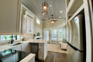 open layout kitchen with view of living room and fireplace. This tiny home comes equipped with stainless steel appliances such as dishwasher and refrigerator
