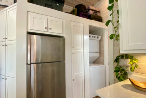 tiny house kitchen apliances including stainless steal refregirator and stackable washer and dryer.