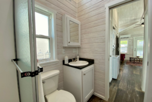 nice size bathroom in tiny home for sale with sink and storage underneath and pharmacy cabinet.