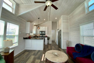 View of the kitchen from the tiny home living room. Open layout concept with darker floors and warm rustic flair.