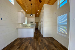 view of kitchen and living space inside tiny home with white walls and large windows.