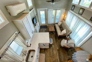 View of the living space and kitchen from tiny home loft. Notice that multiple windows and storage options.