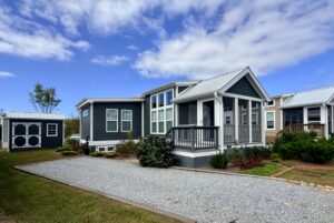A small modern tiny house on Strolling Easy Lane features dark siding, white trim, and a gravel driveway under cloudy skies.