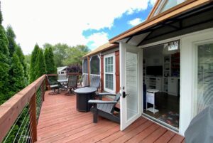 A wooden deck with patio furniture at 40 Drifting Brook Lane, open doors, and trees in the background on a sunny day.