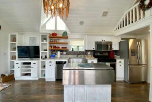 Modern white kitchen on Drifting Brook Lane with stainless appliances, open shelves, and a central island under a chandelier.