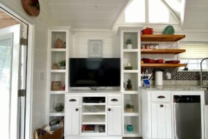 A TV is centered in white built-ins at 40 Drifting Brook Lane, with kitchen shelves and appliances to the right.