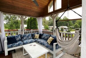 Cozy porch on Drifting Brook Lane with a leafy sofa, white coffee table, hammock chair, and scenic outdoor view.
