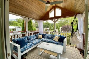 Covered porch with blue-patterned sectional and hammock chair overlooks the leafy neighborhood of Drifting Brook Lane.