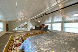 Cozy attic bedroom at 40 Drifting Brook, featuring string lights, a patterned rug, and large windows; ideal real estate find.