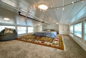 Cozy loft bedroom on 40 Drifting Brook with bed, string lights, bean bag, and colorful rug on carpeted floor.