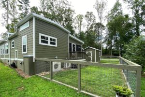 A green house with white trim at 108 Meandering Lane, fenced yard, small shed, surrounded by trees and grass.