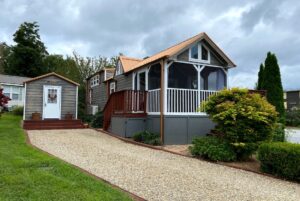 A tiny house with a screened porch and shed sits by a gravel drive at 40 Drifting Brook Lane under a cloudy sky.