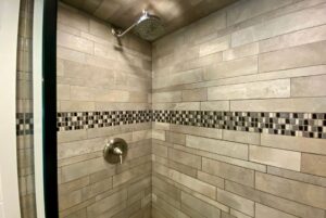 Modern tiled shower at 40 Drifting Brook features a metal showerhead and mosaic tile accent, perfect for real estate appeal.