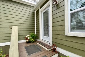Green house entrance at 108 Meandering Lane features a white door, welcome mat, potted plants, and metal dog statue.
