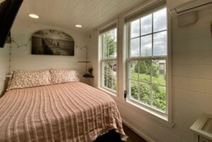 Cozy bedroom at 40 Drifting Brook, with a pink quilt, floral pillows, large windows, and dock photo on white wall.