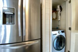 Stainless steel fridge beside a small laundry nook with front-load washer on Drifting Brook Lane.