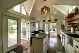 Cozy, bright tiny house interior at 40 Drifting Brook Lane with a kitchen, sitting area, and large windows to greenery.