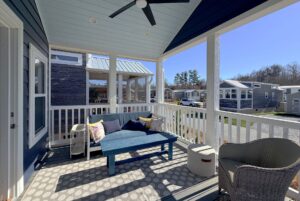 View of a cozy porch with seating and cushions on Skipping Stone Lane, tiny homes in the background on a sunny day.