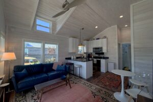 A cozy, modern tiny house living area at 49 Skipping Stone with a kitchen, blue sofa, rugs, and lots of natural light.