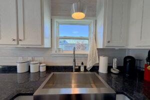 Modern kitchen sink under a window on Skipping Stone Lane, with white cabinets, soap dispensers, and a towel nearby.