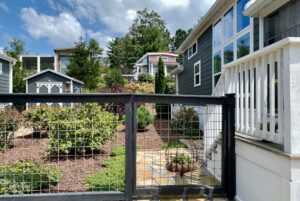 A fenced garden with shrubs and a stone path graces the homes along Just Wandering Lane under a partly cloudy sky.