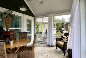 Cozy sunroom with wicker chairs, round table, curtains, and views of gardens and Just Wandering Lane.